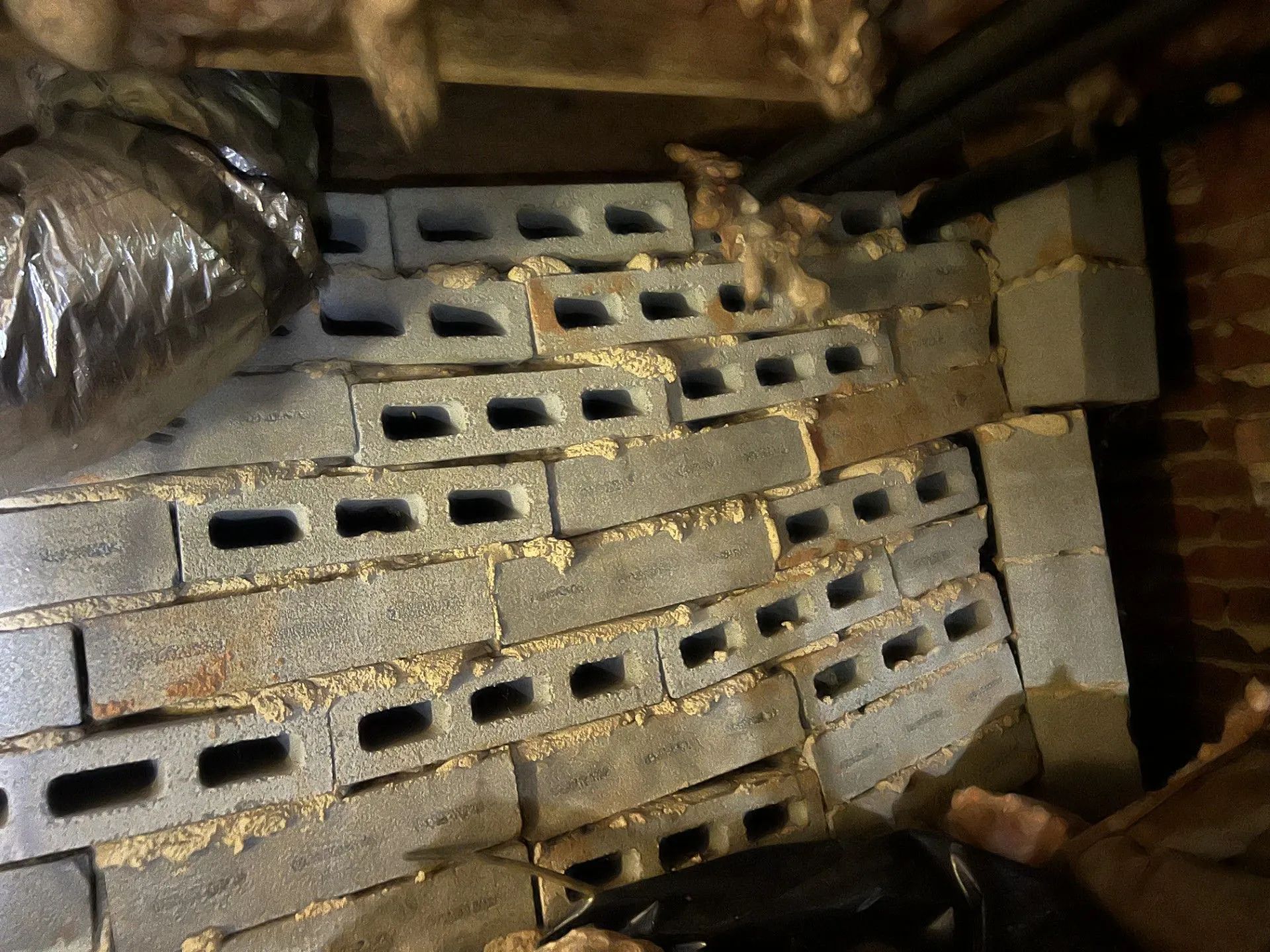 Stack of gray cinder blocks in a cluttered storage area with brick wall and insulation around them