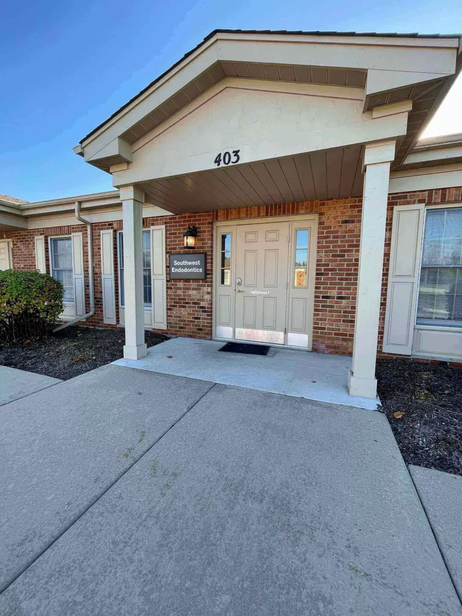 A brick commercial building with a beige covered entrance, white columns, and a double glass door marked number 405.