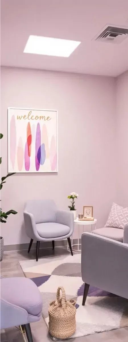 A cozy waiting room with two light-colored armchairs, a patterned rug, a small side table, and abstract wall art.