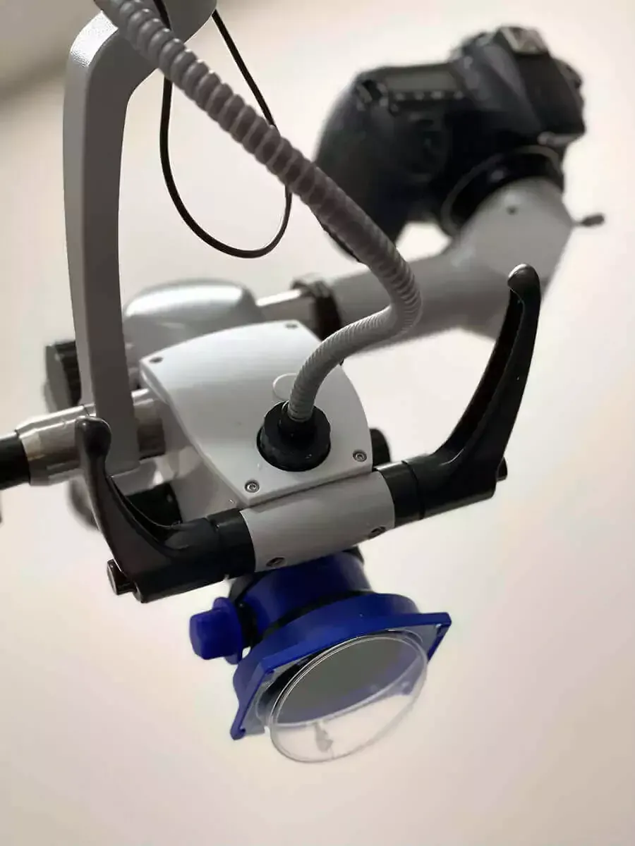 A dental microscope equipped with a camera and a blue protective shield, viewed from a high angle.