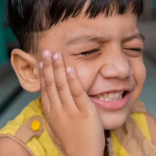 A person with a yellow top holds their hand to their cheek, eyes closed tight in a pained, wincing expression.