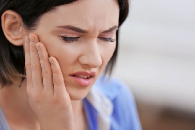 A person with a pained expression holding their hand to their cheek, indicating tooth or jaw pain.