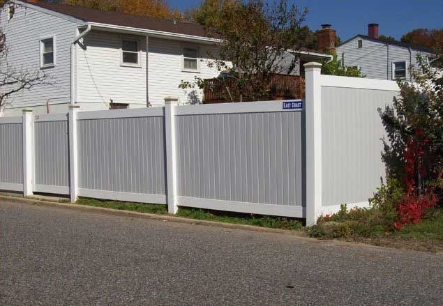 White privacy fence in front of a two-story house on a street.