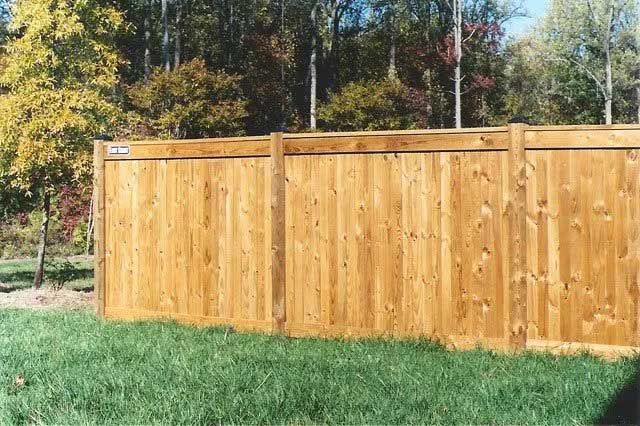 Wooden privacy fence in a grassy yard with trees in the background.