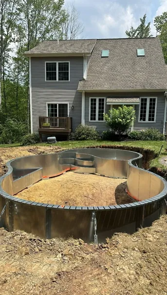 Pool under construction in backyard, metal frame with dirt, house in background.