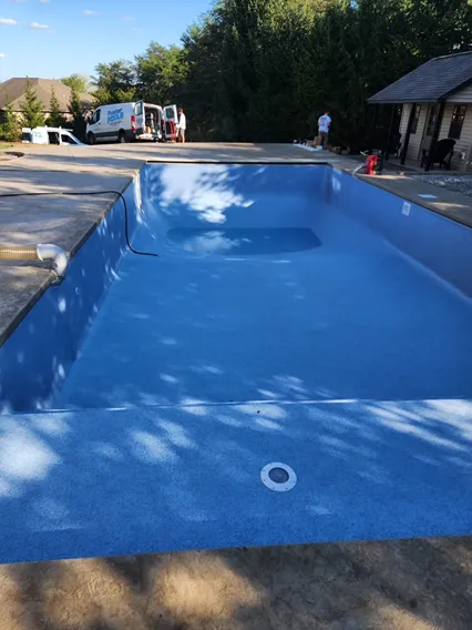 Empty blue swimming pool with concrete surround. Workers and van are in the background.