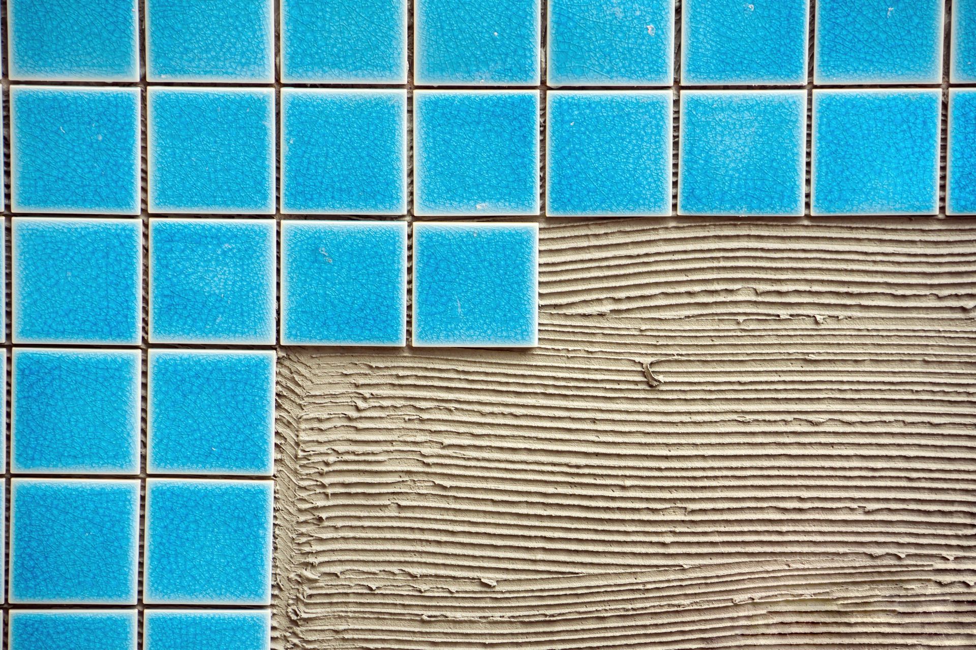 Blue square tiles being installed on a wall with grey adhesive visible.