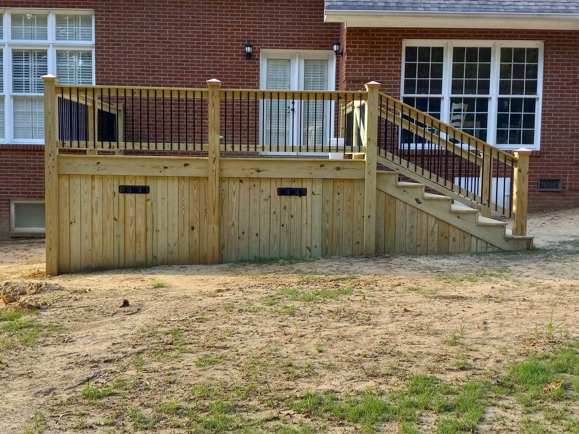 Wooden deck with stairs, black railing, and storage compartments attached to a brick house.