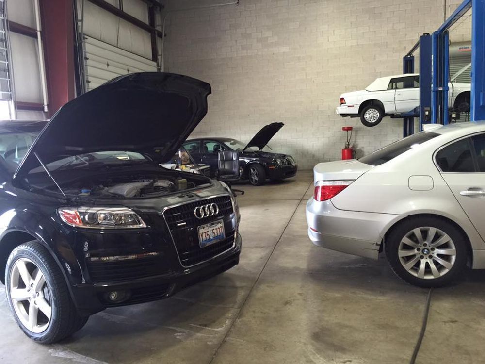 Cars in a repair shop with hoods open; one on a lift.