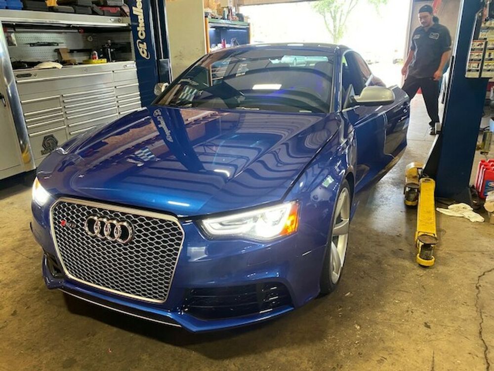 Blue Audi RS5 coupe in a garage; a mechanic stands nearby.