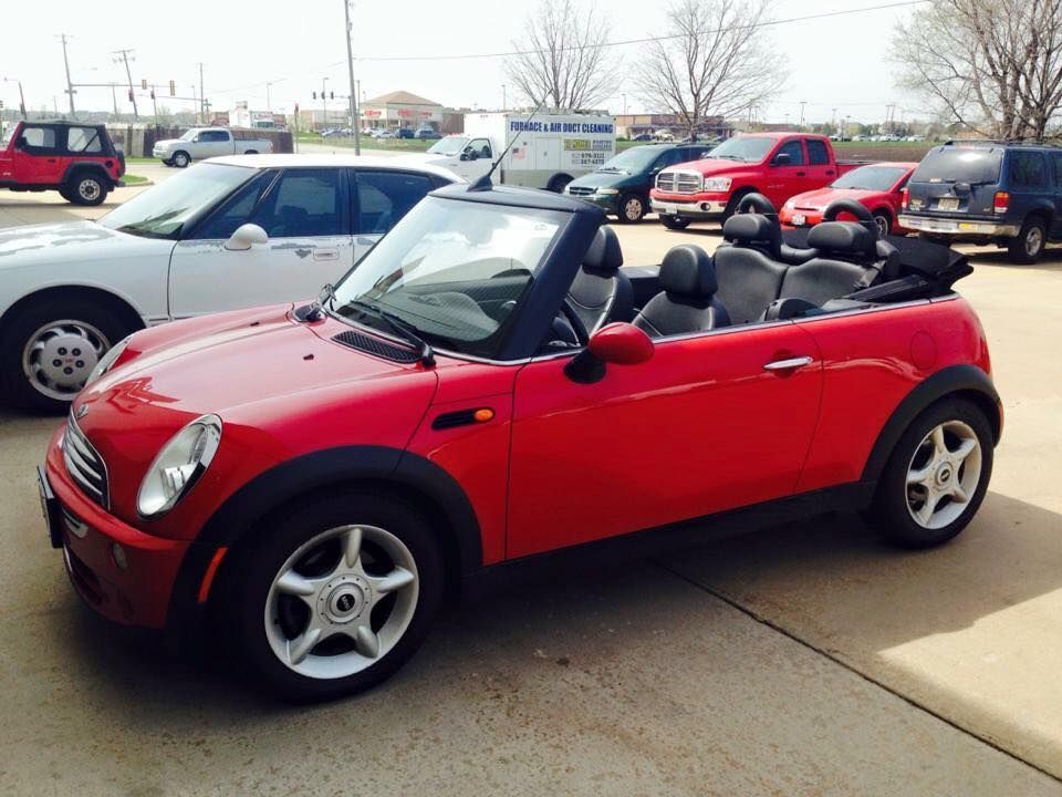 Red convertible Mini Cooper parked in a lot, top down. Other cars visible in the background.