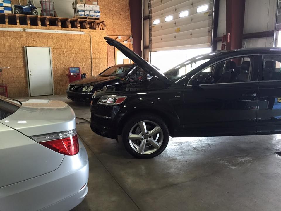 Cars in an auto repair shop: silver sedan, black SUV with hood open, and a car in the background.