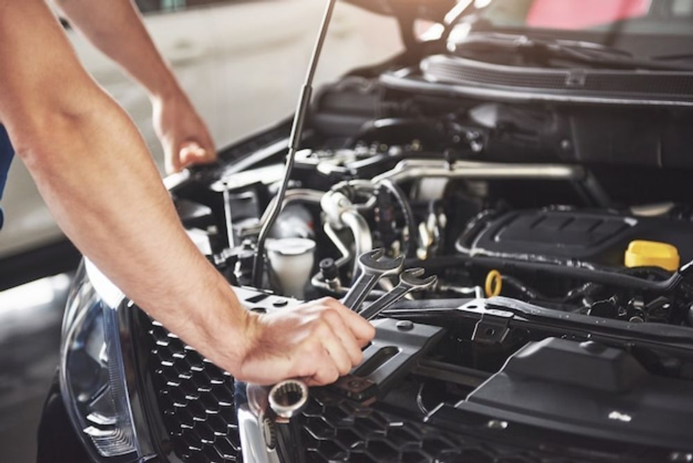 Mechanic working on a car engine with a wrench, in a garage.