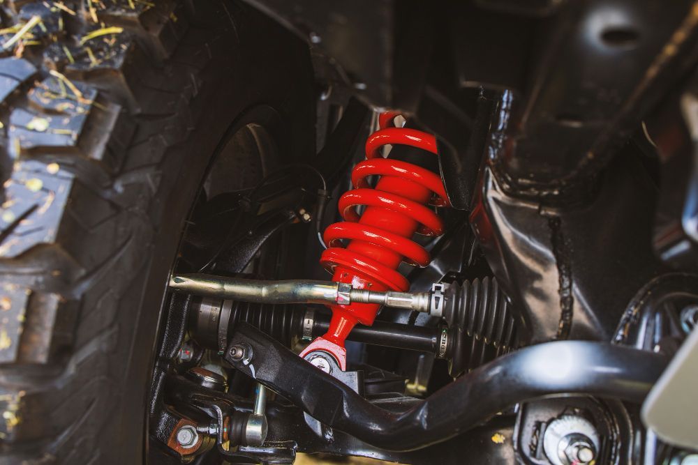 Red coil-over shock absorber on a vehicle's suspension system, with a black frame and tire.