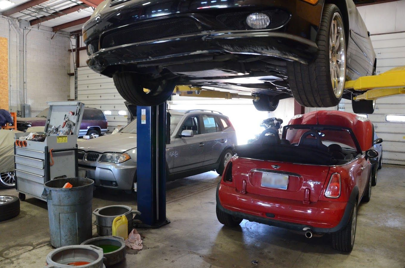 Car repair shop: Black car on a lift, red Mini Cooper, gray SUV, tools, and a cluttered interior.