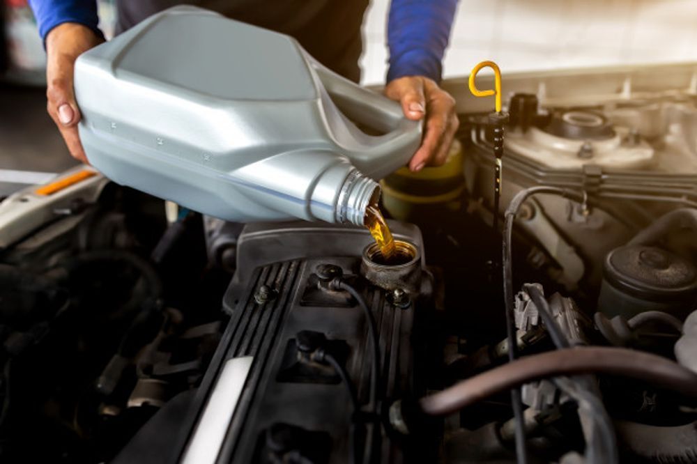 Person pouring motor oil into a car engine in a garage.