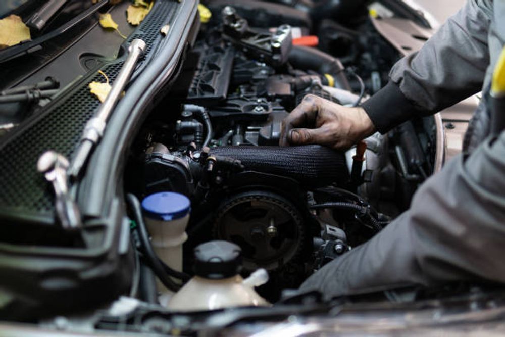 Mechanic working on a car engine, hands on black engine components.