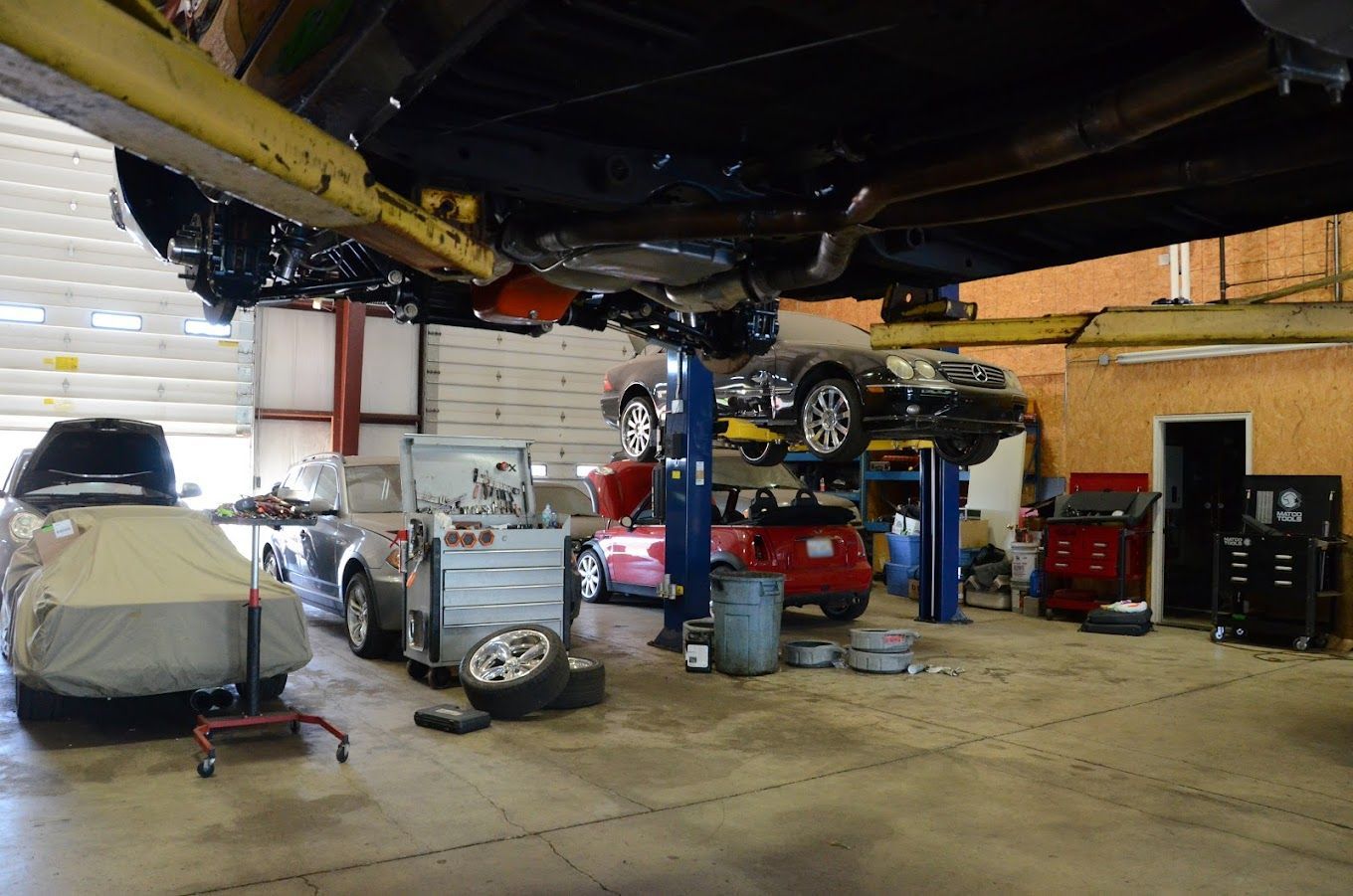 Garage interior with cars on lifts, mechanics working. Tools and equipment scattered throughout the shop.