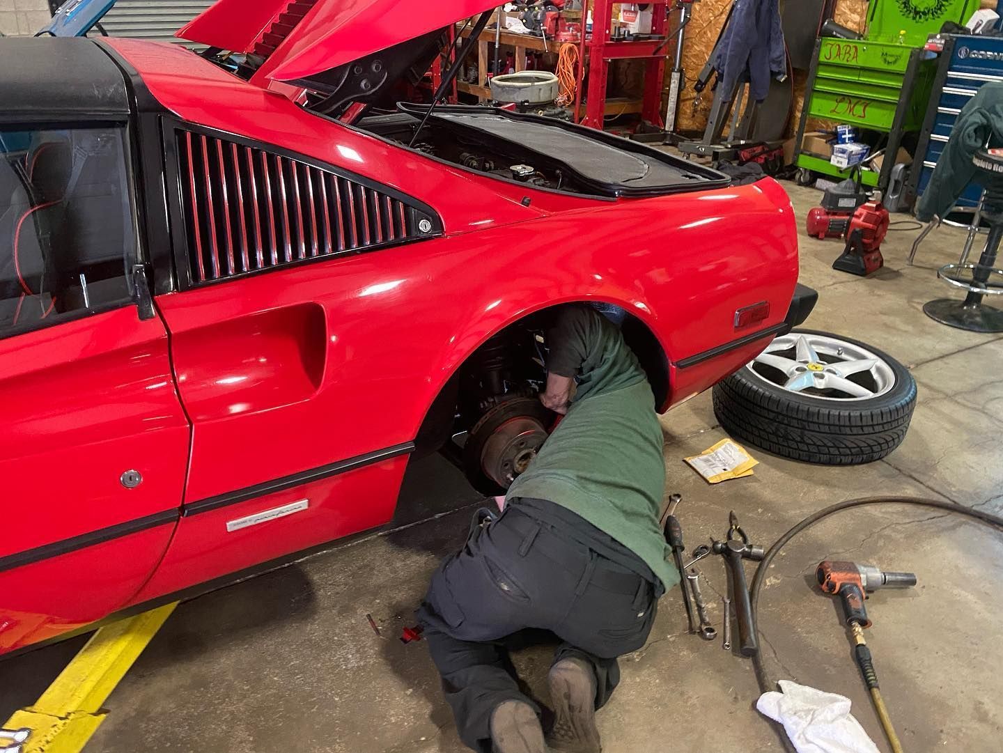Mechanic working on the rear wheel of a red Ferrari in a garage.