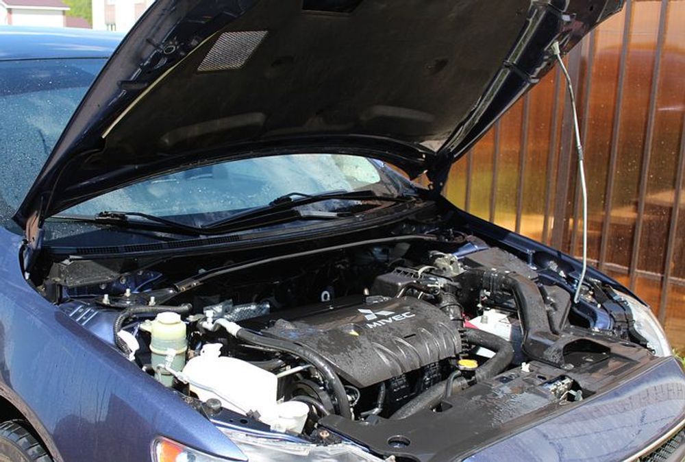 Blue car with open hood, engine compartment being cleaned with water.