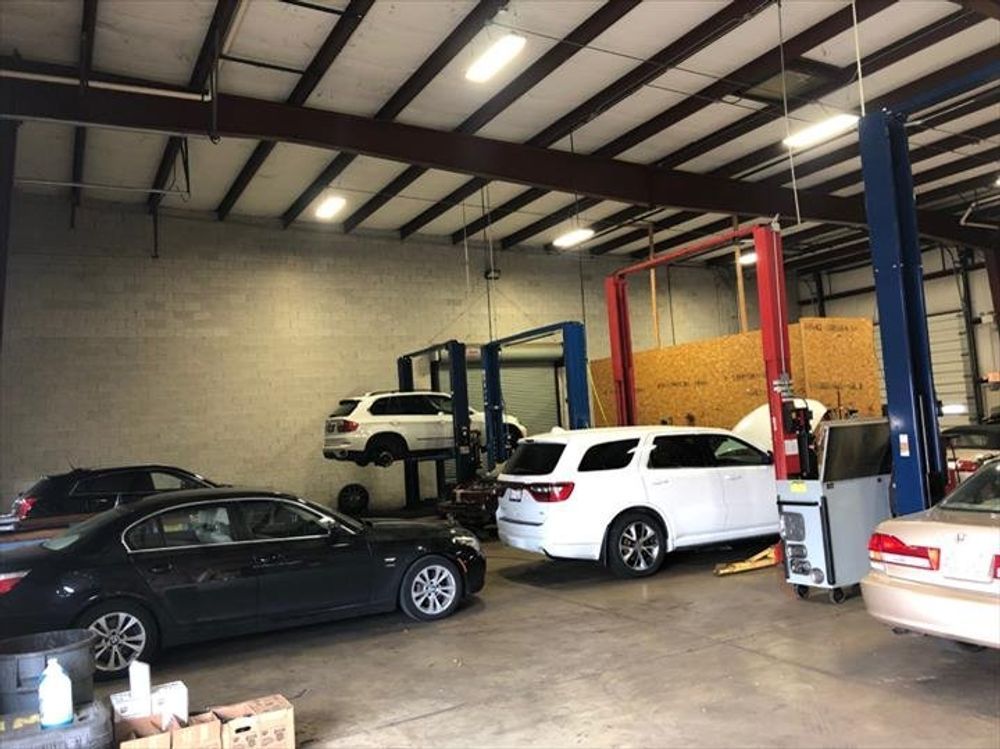 Cars in a garage, two SUVs on lifts. Other cars on the ground, tools and equipment visible.