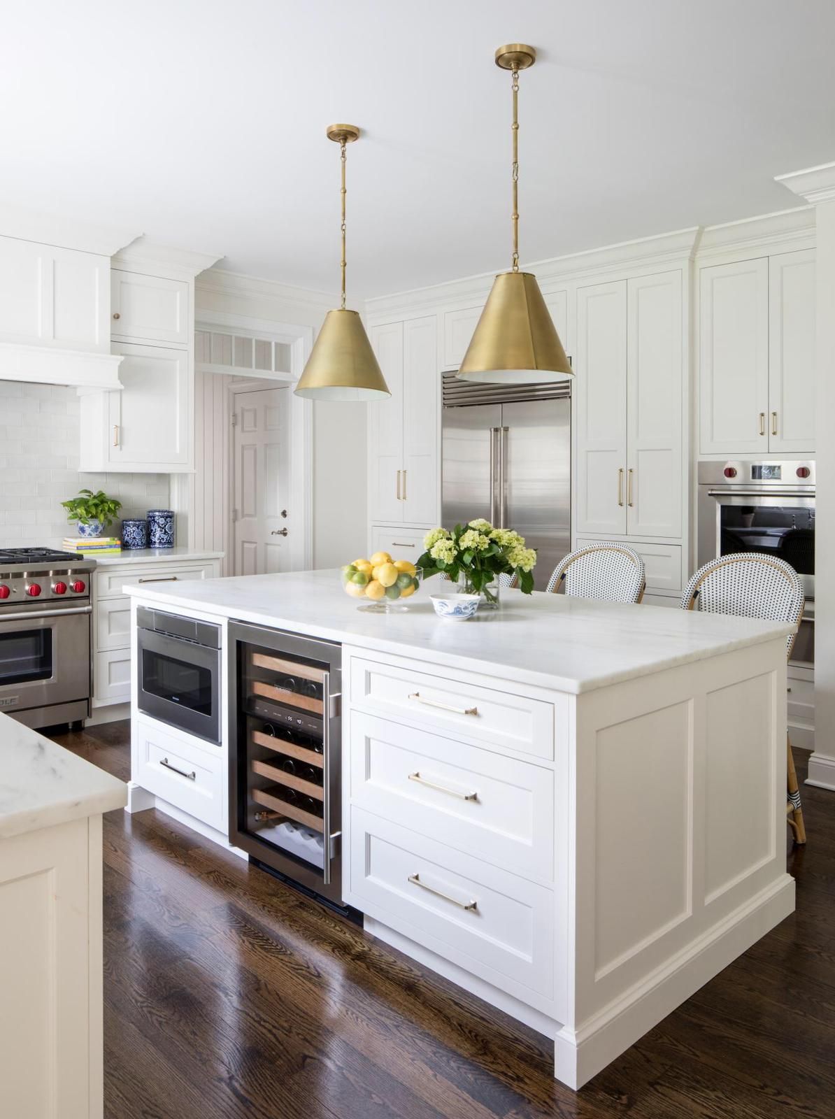 A kitchen with white cabinets, stainless steel appliances a large island, and a wine cooler.