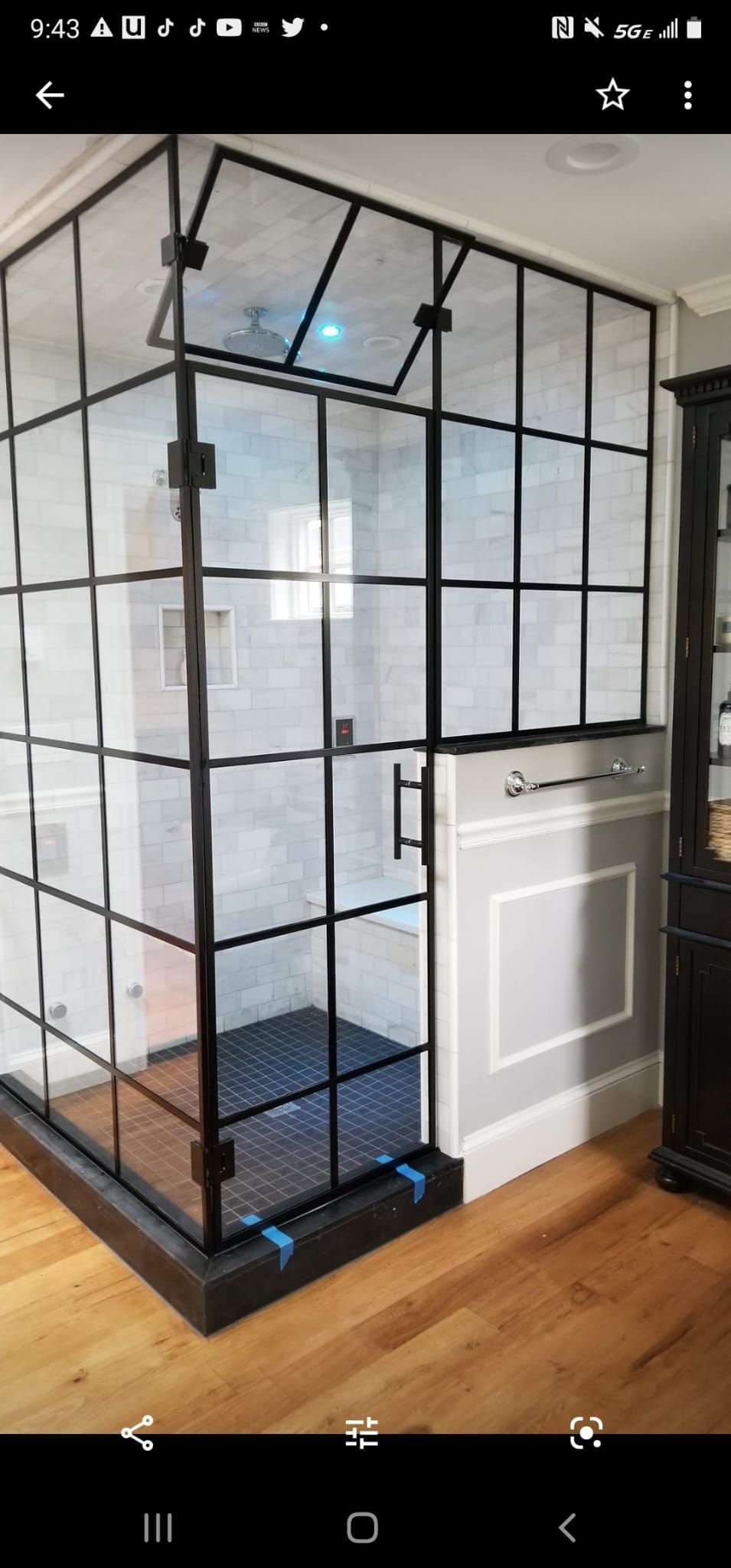 A bathroom with a walk in shower with a black frame.