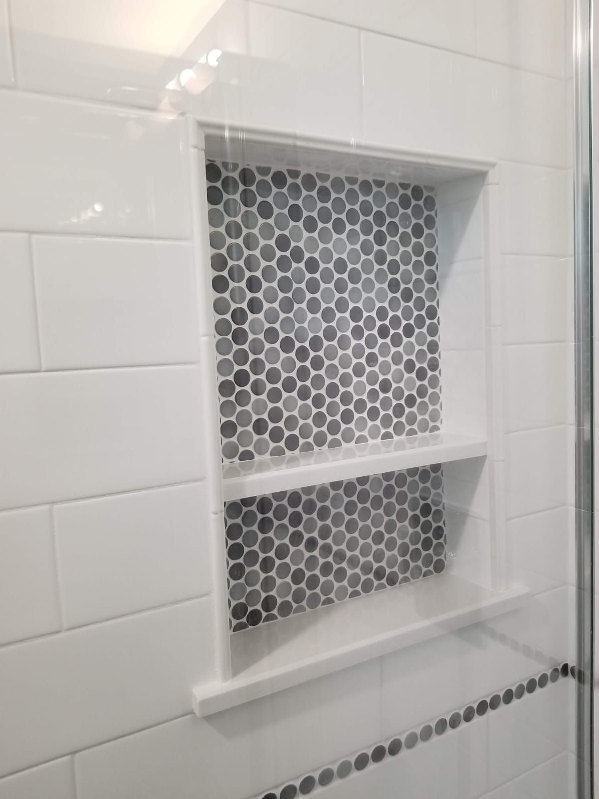A bathroom with white tiles and a shower niche with black and white tiles.