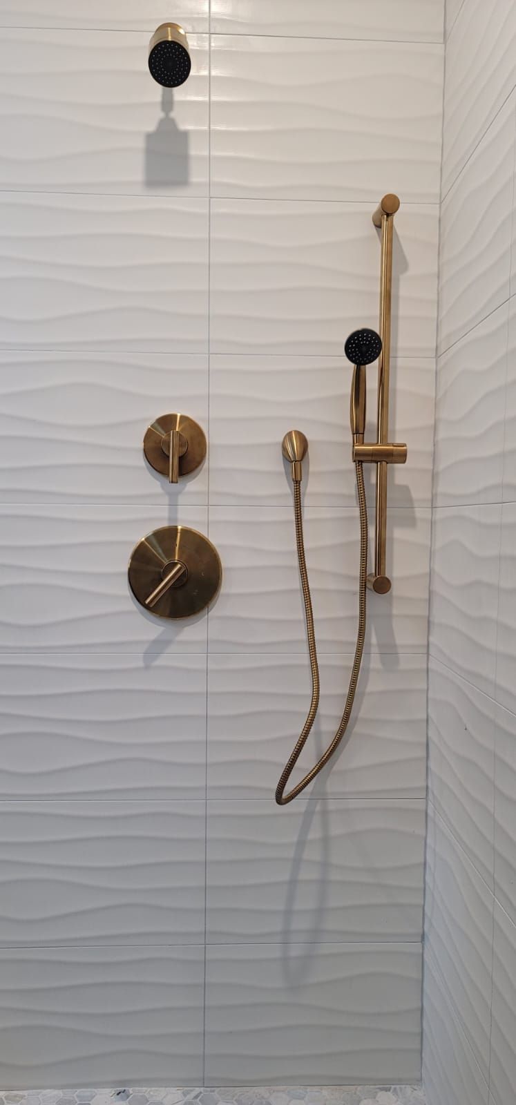 A shower with a brass shower head and faucets on a white tiled wall.