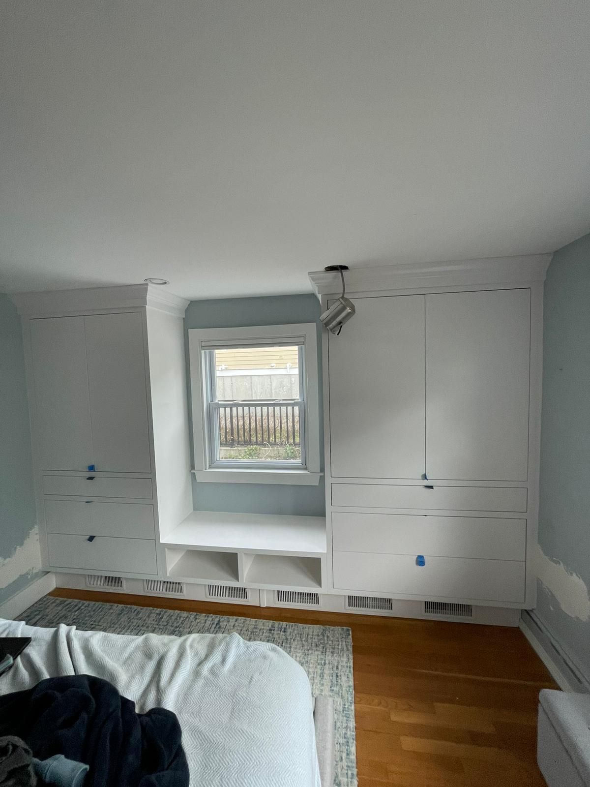 A picture of a bedroom with a bed, dressers, drawers, and a window.