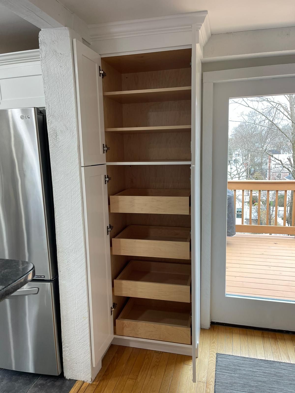 A pantry with drawers and shelves in a kitchen next to a sliding glass door.