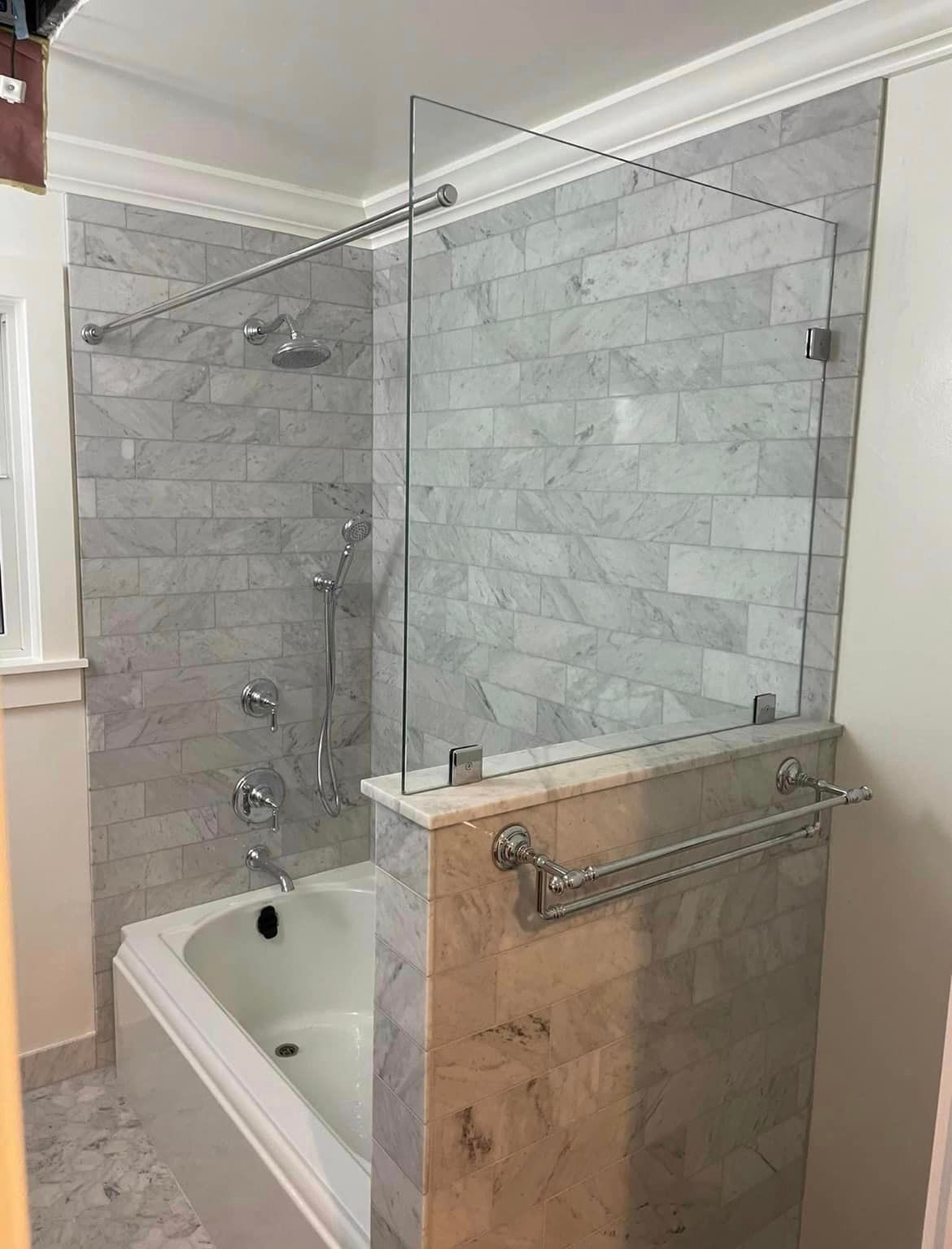 Bathroom with marble tile walls, a white bathtub, and glass shower screen.