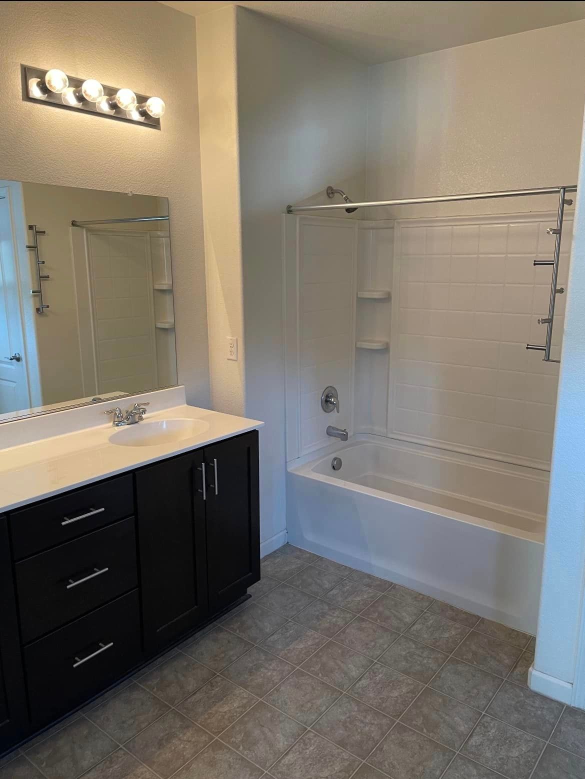 Bathroom with a dark vanity, white tub, and a large mirror. Beige flooring.