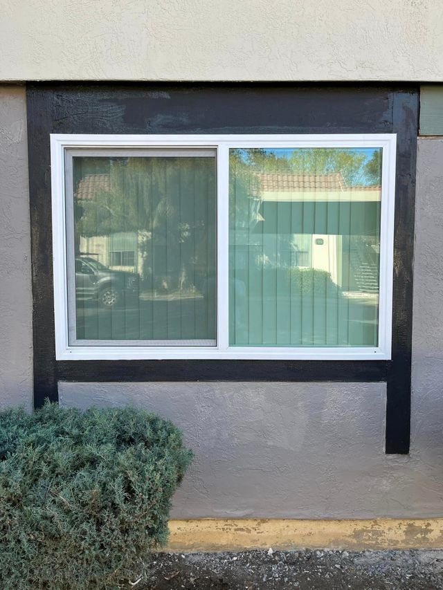 Sliding window with white frame, surrounded by black trim on a beige wall, reflecting outdoor scene.