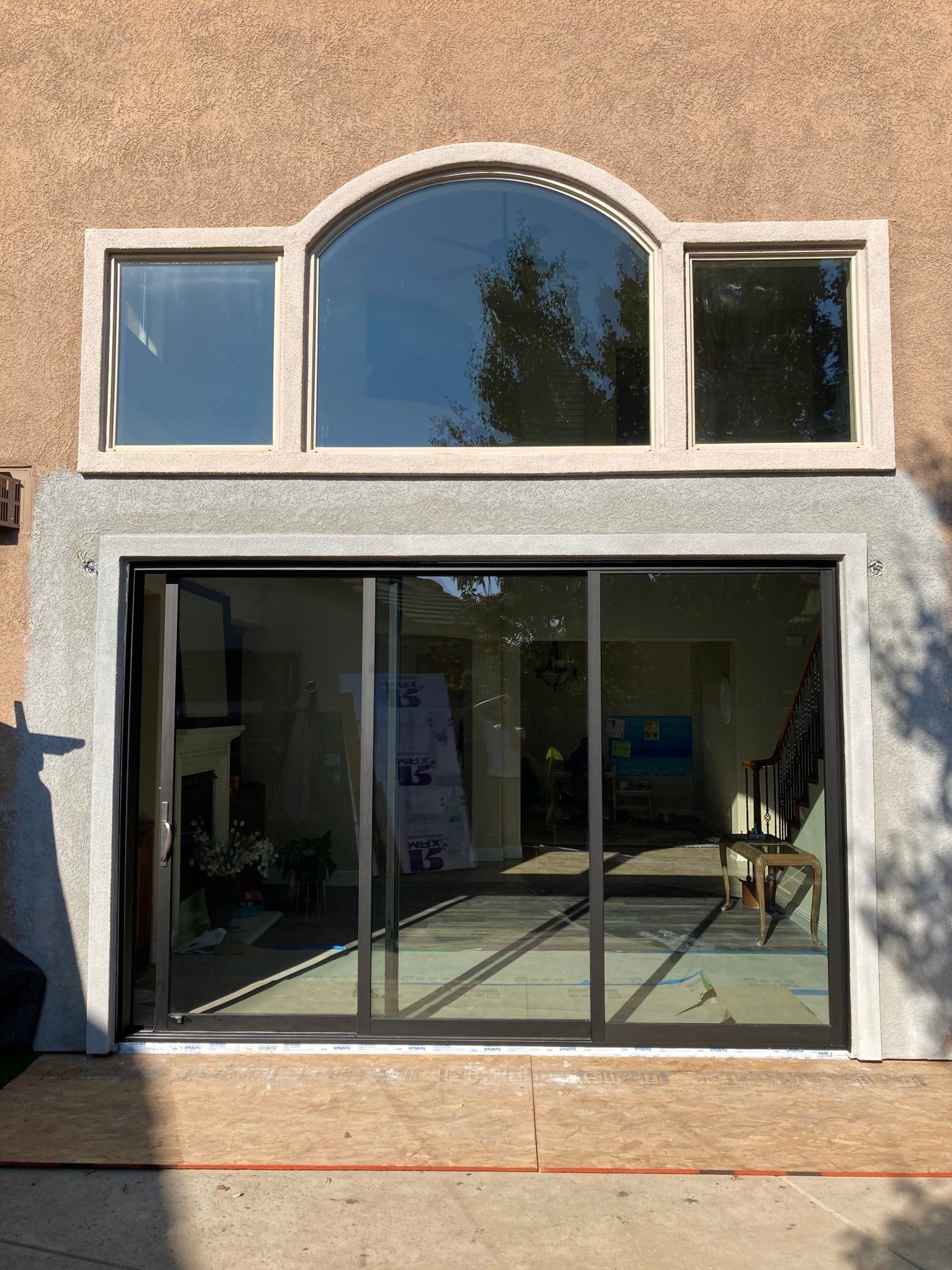 Exterior view of a house with large sliding glass doors below a trio of windows, one arched.