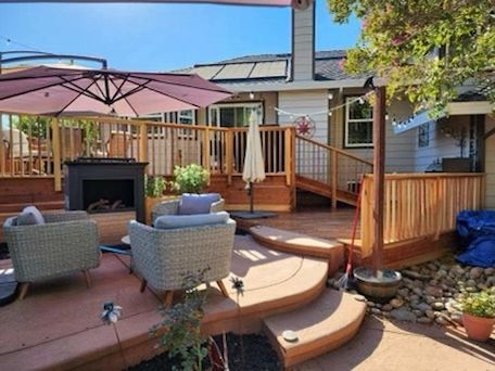 Wooden deck with seating areas, fireplace, and umbrella; house in the background.