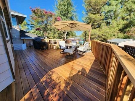 Wooden deck with outdoor furniture under a patio umbrella, surrounded by trees.