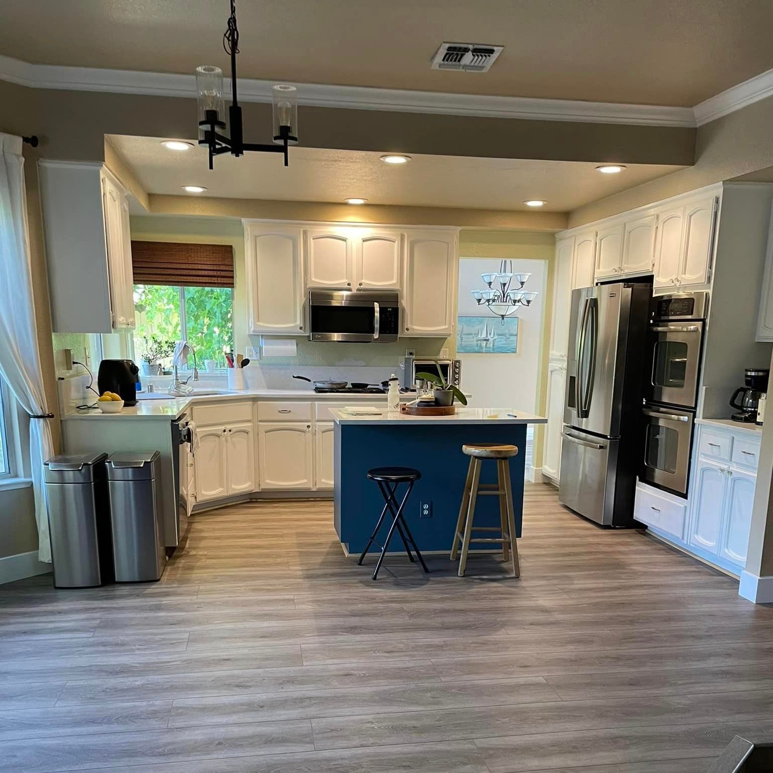 Kitchen with white cabinets, blue island, stainless steel appliances, and wooden floors.