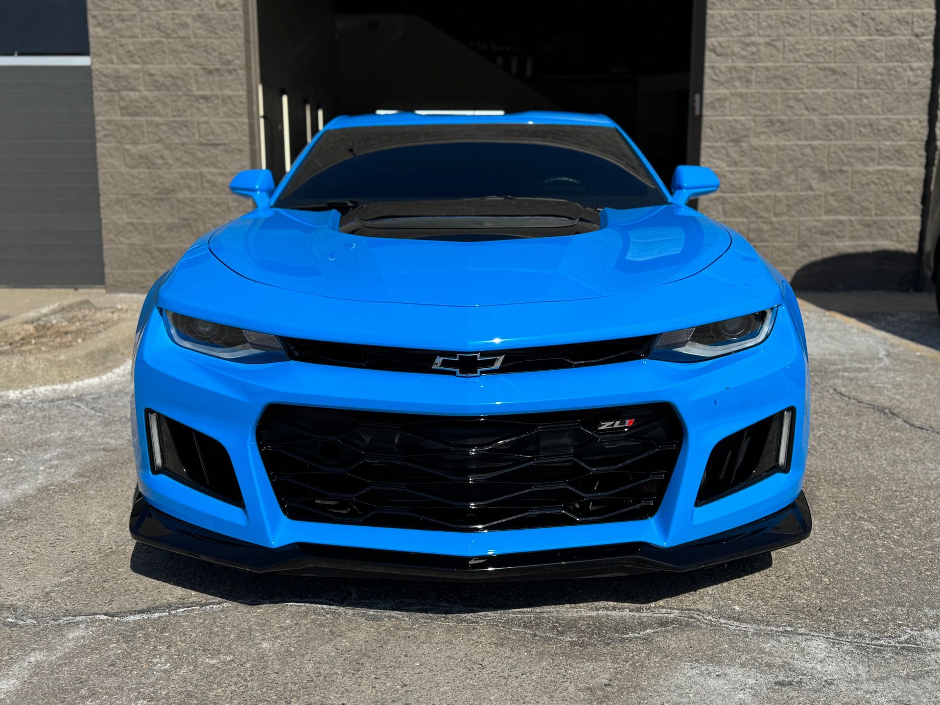A technician wearing white gloves uses a red squeegee to apply a clear protective film to a glossy gray car panel.