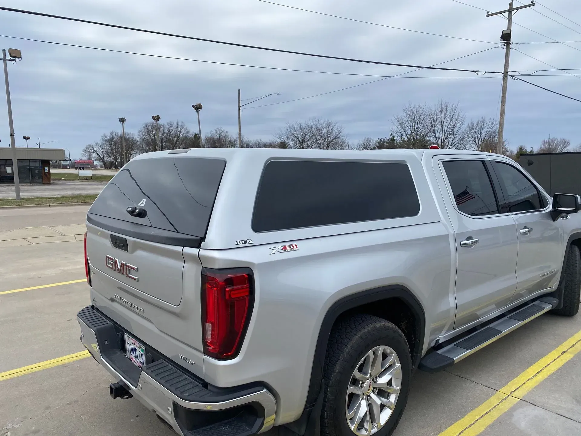 Silver pickup truck with a cap parked in a parking lot on a cloudy day.