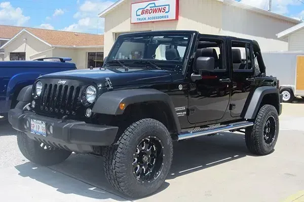 Black Jeep Wrangler with black rims parked outside a building with a sign.