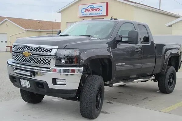 Dark gray lifted Chevrolet Silverado pickup truck parked in front of an auto shop.