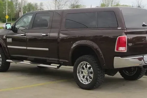 Brown pickup truck with a cap on a paved surface. Chrome wheels, running boards, and a shiny bumper.