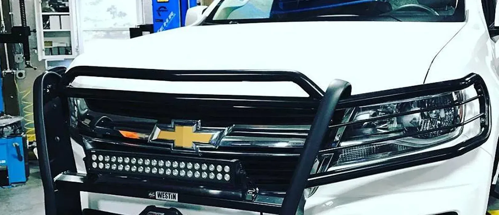 White Chevrolet truck with black grill guard and light bar.