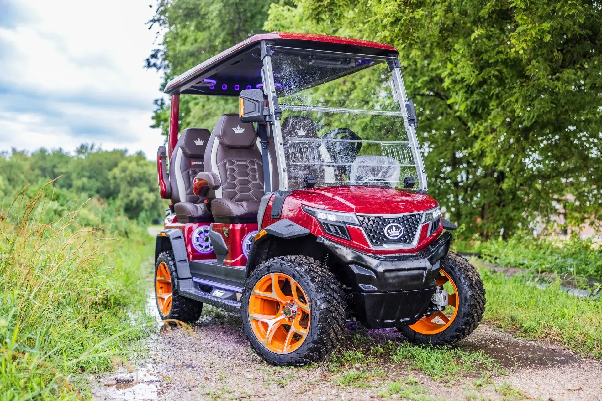 Red and orange golf cart with clear windshield on a grassy path.