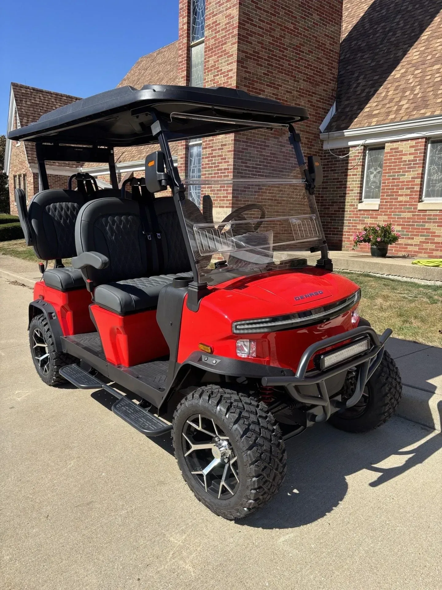 Red and black golf cart with upgraded tires parked on pavement.