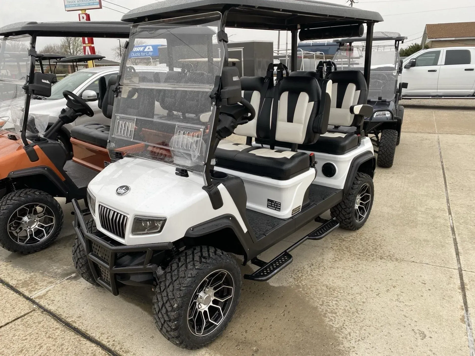White and black golf cart with four seats, black wheels, parked outdoors.
