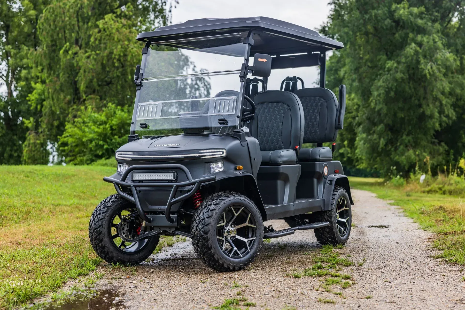 Black golf cart with large wheels on a gravel path near trees.