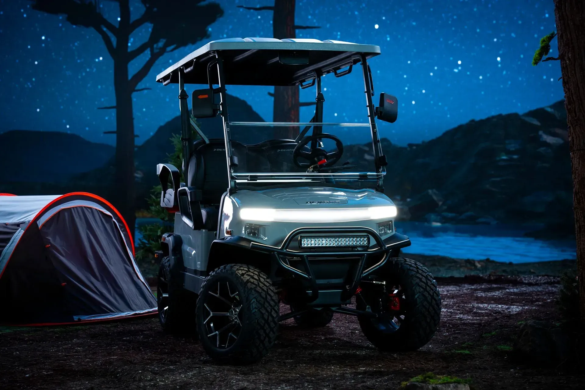 Off-road golf cart with bright headlights near a tent and lake under a starry night sky.