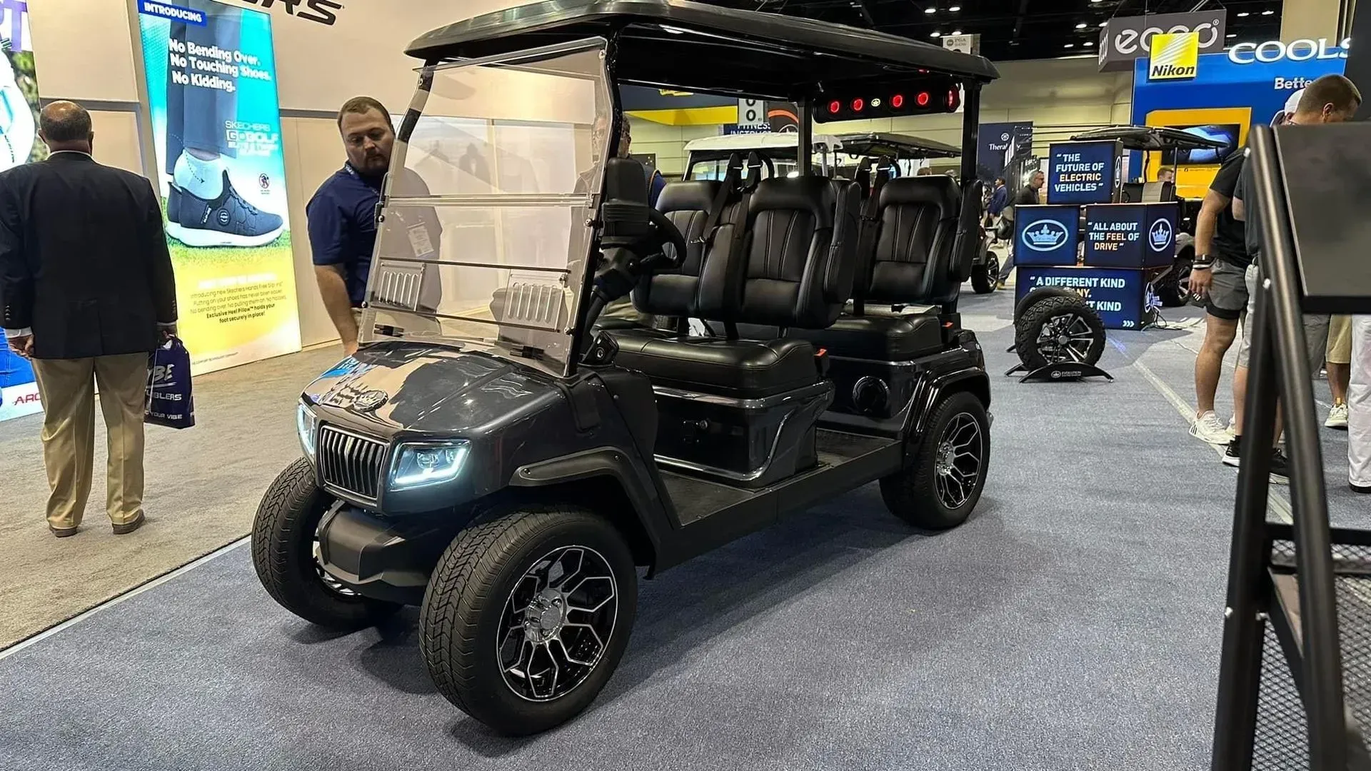Black golf cart on display at a trade show, with a man looking at it.